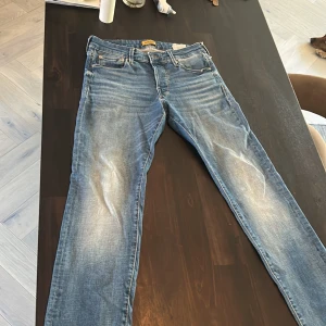 Blå jeans från Jack & Jones - Snygga blå jeans från Jack & Jones med klassisk femficksdesign och slitna detaljer framtill. Jeansen har normal passform och raka ben, tillverkade i mjukt denimtyg med ljusa tvättade partier för en cool look.