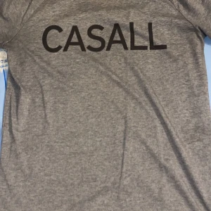 Grå t-shirt från Casall - Snygg grå t-shirt från Casall med svart logga framtill. Klassisk passform och tillverkad i mjuk bomullsmix, perfekt för träning eller chill. Enkel och stilren design som funkar till det mesta.