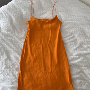 Orange tight klänning från Dilvin - Säljer en orange kort klänning från Dilvin med smala axelband och figurnära passform. Klänningen är ärmlös och har en enkel, stilren design i mjukt bomullsmaterial. Perfekt för dig som gillar färg och vill sticka ut lite extra.