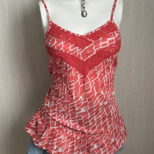 Röd och vit mönstrad linnetopp - Snygg röd och vit linnetopp från Odd Molly med smala axelband, spetsdetaljer i rött och ett unikt grafiskt mönster. Toppen har volang nertill och smock i ryggen för skön passform. Perfekt för varma dagar och somriga vibes.