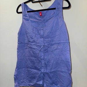 Blå ärmlös blus - Säljer en blå ärmlös blus från Esprit. Toppen har knappar framtill, dekorativa sömmar och ett knytband i midjan för extra passform. Enkel att styla med jeans eller shorts.