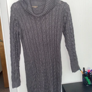 Grå stickad långklänning med polokrage - Säljer en mysig grå stickad långklänning med polokrage och kabelstickat mönster. Klänningen har långa ärmar och är perfekt för kyliga dagar. Den har en loose passform och känns både stilren och bekväm.