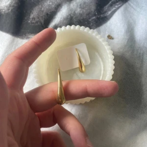 Guldiga droppformade örhängen/ 18 k guldpläterade  - Säljer ett par stilrena örhängen i guldig färg med droppformad design.  Köpta i Turkiet! De är släta och blanka, vilket ger en modern och trendig look. Perfekta för dig som gillar minimalistiska smycken med en twist.