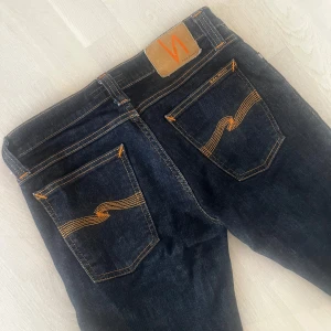 Mörkblå jeans från Nudie Jeans Co - Säljer ett par mörkblå jeans från Nudie Jeans Co med klassiska orange sömmar och snygg broderad detalj på bakfickorna. Jeansen är w29 L32 tight long John nästan helt nya ny pris 1600 mitt pris 299 kan se lite svarta på en bilden men de är mörk blå (om några frågor kontakta mig) 