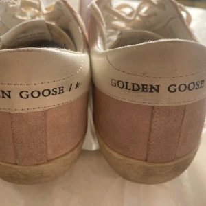 Golden Goose rosa sneakers i mocka - Golden Goose sneakers i ljusrosa mocka med vit stjärna på sidan och vita skinnpartier vid hälen. Klassisk rund tå, vita snören och platt sula. GGDB-logga på plösen och hälen. Stora i storleken, passar 38or.