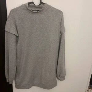 Grå sweatshirt med hög krage - En enkel och stilren grå sweatshirt med hög krage och långa ärmar. Tröjan har en loose passform och är tillverkad i mjuk bomullsmix, perfekt för chill dagar. Snygga detaljer vid axlarna ger en modern touch.