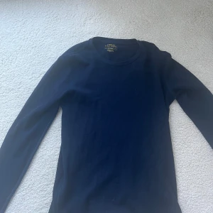 Mörkblå långärmad tröja Polo Ralph Lauren - Mörkblå långärmad tröja från Polo Ralph Lauren med röd broderad logga på bröstet. Tröjan är ribbad och har en klassisk rund halsringning. Perfekt för dig som gillar stilrena och tidlösa plagg med premiumkänsla.