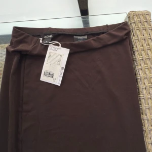 Brun långkjol från Monki XS - Säljer en stilren brun långkjol från Monki i storlek XS. Kjolen har en rak och tight passform som sitter snyggt längs kroppen. Tillverkad i mjuk bomullsmix med stretch för extra komfort. Helt oanvänd med lappen kvar. Säljer pga förliten 