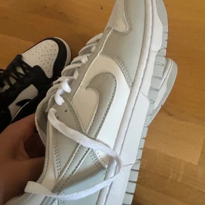 Nike Dunk sneakers svart/vit & grå/vit - Två par Nike Dunk sneakers säljes! Ena paret är svart och vitt med klassisk kontrast, det andra är i stilren grå och vit färg. Båda har perforerad tå, snörning och den ikoniska swoosh-loggan på sidan. Perfekta för dig som gillar streetstyle och vill ha något fräscht till vardags.