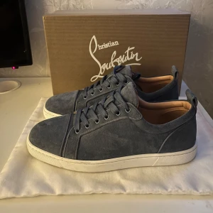 Äkta blå sneakers från Christian Louboutin - Säljer ett par snygga blå sneakers från Christian Louboutin i mocka. De har en klassisk design med snörning och en röd sula som ger en stilren look. Perfekta för både vardag och festliga tillfällen. Skorna är i mycket bra skick och kommer med originalkartong. Skorna är även äkta 