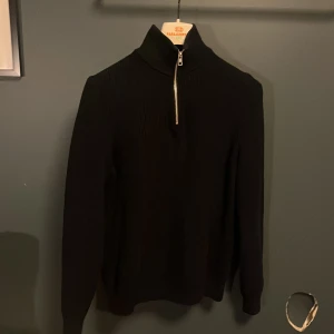 Svart stickad polotröja från Zara - Svart stickad polotröja från Zara med ribbad struktur och half zip-dragkedja framtill. Hög krage och långärmad modell som ger en clean och stilren look. Perfekt för lager-på-lager under kyliga dagar.