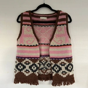 Stickad väst från Odd Molly med mönster - Superfin stickad väst från Odd Molly i brunt, rosa och beige med coola mönster och fransar nedtill. Västen har breda axelband, öppen front och är perfekt för lager-på-lager. Färgglada ränder och grafiska detaljer gör den unik och riktigt snygg.🤩💕