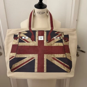 Ny stor shoppingväska med Union Jack-tryck - Helt ny, unik snygg och rymlig shoppingväska i beige bomullscanvas med stort Union Jack-tryck. Du får plats med massor där i. Väskan har dubbla handtag, 4 innerfack och 2 innerfack med dragkedja. Magnetknäppning upptill. Cool brittisk vibe! Hämtas i Hägersten om du vill slippa frakt. Var även uppmärksam på när Plick erbjuder fraktfritt ibland på dyrare plagg. Följ mig gärna. Har mycket att lägga ut i olika storlekar! 