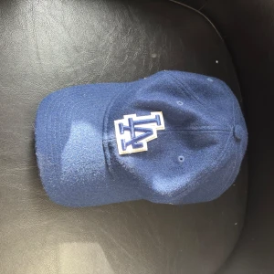 Blå LA Dodgers keps från New era - Snygg blå LA Dodgers keps från New Era 9TWENTY-serien. Kepsen har broderad LA-logga framtill i blått och vitt, böjd skärm och justerbar rem baktill. Tillverkad i en mix av ull och polyester. Knappt använd och utan defekter såsom fläckar, små revor osv.