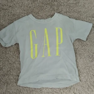 GAP t-shirt med neontryck - Ljusgrå t-shirt från GAP med stort neongult logotryck på bröstet. Klassisk rund hals och korta ärmar. Står storlek L men passar precis som en S tshirt skulle jag säga, jag brukar ha xs-s och denna är perfekt.