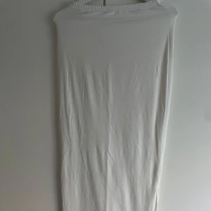 Vit långklänning med knyt - Säljer en vit kjol med slät yta och mjukt, tunt tyg. Kjol  har knytband i sidorna som ger en cool detalj och gör att du kan justera passformen. Enkel och stilren design, perfekt för dig som gillar minimalistiskt mode.