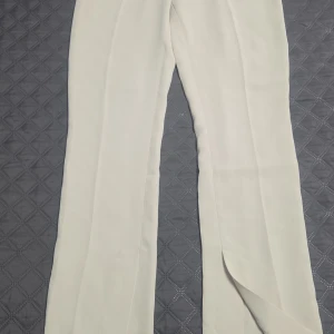 Vita raka kostymbyxor - Stilrena vita kostymbyxor med raka ben och pressveck. Byxorna har en klassisk look och är tillverkade i ett lätt tyg som ger en snygg siluett. Perfekta för dig som gillar en clean och fräsch stil.