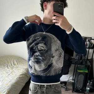 Mörkblå tröja med stort ansikte, Soul London - Unik mörkblå tröja från Soul London i storlek S med ett stort, detaljerat ansikte i vitt på framsidan. Tröjan har rund halsringning och långa ärmar. Perfekt för dig som vill sticka ut med en cool och konstnärlig look.