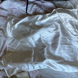 Vit satin blus från SHEIN - Säljer en vit blus från SHEIN i satinliknande material. Blusen har tunna axelband och en liten slits på sidan med snören man kan göra en lite knut med. Aldrig använd då den va för stor på mig. 