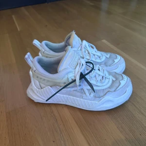 Off-White vita sneakers med snörning - Säljer ett par feta vita Off-White sneakers med klassisk pil-logga på sidan och coola detaljer som den ikoniska zip-tagen. Skorna har mesh och skinnpaneler, grov sula och röda sömmar på hälen. Perfekta för dig som vill sticka ut med streetstyle.
