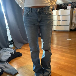 Ljusblå raka jeans med hål på knät - Säljer ett par ljusblå jeans med rak passform och klassisk femficksdesign. Jeansen har ett snyggt hål på ena knät för en trendig look. De är midwaist och tillverkade i jeansmaterial. Perfekta för dig som gillar en avslappnad och cool stil.