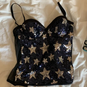 Svart paljettkorsett med stjärnor Intimissimi - Supersnygg svart korsettopp från Intimissimi täckt med glittriga silverpaljetter i stjärnform. Toppen har smala axelband, markerade kupor och croppad passform. Perfekt för att sticka ut med sitt stjärnmönster och glittriga look. aldrig använt 