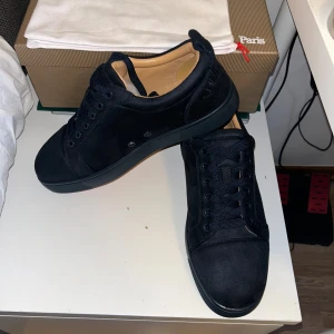 Mörkblå sneakers från Christian Louboutin - Säljer ett par svarta sneakers från Christian Louboutin i mocka med klassisk röd sula och diskreta metalldetaljer på sidan. Skorna har rund tå, snörning och en stilren design som passar perfekt till streetwear eller en mer dressad look.