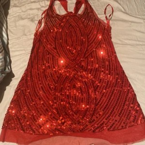 Röd paljettlinne från A'gaci - Supersnygg röd paljettlinne från A'gaci med glittriga paljetter i geometriskt mönster. Linnet  har halterneck med knyt i nacken och är ärmlös. Perfekt för dig som vill sticka ut med en riktigt glammig look.