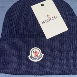 Moncler mössa - Snygg mörkblå mössa från Moncler med klassisk ribbstickad struktur och broderad logotyp framtill. Tillverkad i mjuk ull som håller dig varm under kalla dagar. Perfekt accessoar för att lyfta din vinterstil. skriv för fler bilder