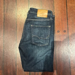 Jack & Jones mörkblå tapered jeans - Mörkblå jeans från Jack & Jones med snygg tvätt och klassiska kontrastsömmar. Modellen är Tapered/Mike med avsmalnande ben och femficksdesign. Jeansen har läderpatch bak i midjan och är tillverkade i slitstarkt denimtyg.