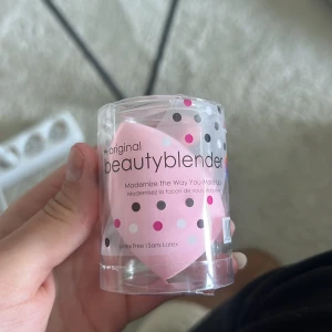 Original rosa Beautyblender - Säljer en original Beautyblender i ljusrosa färg. Den kommer i sin genomskinliga förpackning med prickigt mönster. Perfekt för att applicera foundation, concealer eller andra basprodukter. Tillverkad i mjukt, latexfritt material för en flawless finish.