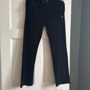 Svarta Juicy Couture mjukisbyxor S - Svarta mjukisbyxor från Juicy Couture i velour med strassdetaljer. Byxorna har normal passform, resår i midjan och fickor fram. På baksidan står det 'Juicy' i stora strasstenar och framtill finns en liten logga i strass.
