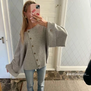 Grå oversized kofta med knappar - Säljer en grå oversized kofta med breda ärmar och snygg asymmetrisk knäppning framtill. Koftan har stora träknappar och är stickad i mjukt material, perfekt för att ge en chill och trendig vibe till din outfit.