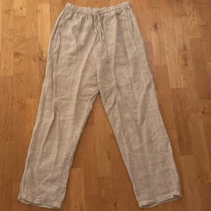 Beiga linnebyxor med dragsko - Säljer ett par ljusa beiga linnebyxor med avslappnad passform och elastisk midja med snörning. Perfekta för varma dagar och chill vibes. Byxorna har raka ben och sidofickor för en enkel och clean look.