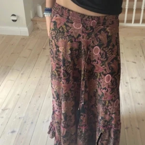 Blommig långkjol från Philosophy - Supersnygg långkjol från Philosophy med blommigt mönster i rosa, lila och grönt på svart botten. Kjolen har resår i midjan och knytband med tofsar. Perfekt för dig som gillar boho-vibe och vill ha något flowy och bekvämt.