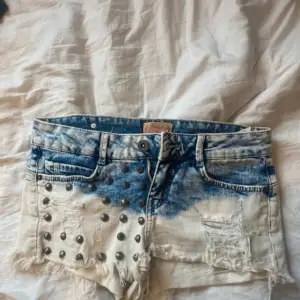Säljer ett par snygga jeansshorts från Bershka i blå och vit tvättad denim. Shortsen har råa kanter, slitningar och coola nitar framtill. Klassisk femficksmodell med knapp och dragkedja. Perfekta för sommaren!
