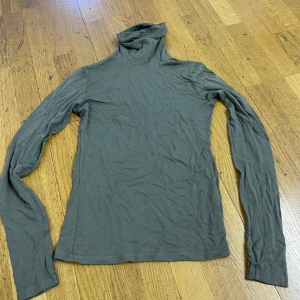 Grå polotröja från Indiska - Mjuk och tunn grå polotröja från Indiska med lång ärm och klassisk hög krage. Perfekt att styla lager på lager eller bära som den är. Enkel och stilren design som funkar till allt. Materialet känns lätt och smidigt mot huden.