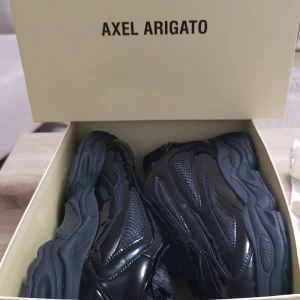 Svarta sneakers Axel Arigato x GmbH - Chunky svarta sneakers från Axel Arigato i samarbete med GmbH. Skorna har en futuristisk design med glansiga paneler i syntet och mesh-detaljer. Tjock sula och snörning framtill. Perfekta för dig som vill sticka ut med en modern streetstyle.Skoren är helt nytt och oanvänd. 