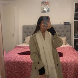 Beige trenchcoat med svarta knappar - Snygg beige trenchcoat med klassisk krage och svarta knappar framtill. Jackan har en längre, loose passform och är perfekt för lager-på-lager.  den har detaljer som knappar vid ärmslut och axlar. Jag köpte den för 1300kr från Åhléns men vill sälja den den är ganska ny här knappt använt den 