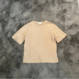 Beige t-shirt i bomull - En enkel och stilren beige t-shirt med korta ärmar och rund hals. Tillverkad i mjuk bomull som känns skön mot huden. Perfekt för dig som gillar minimalistisk och clean stil. Passformen är normal och t-shirten är lätt att matcha med andra plagg.