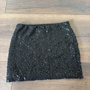 Svart paljettkjol från Boohoo - Snygg svart kortkjol från Boohoo, täckt med glittriga paljetter som ger en riktigt festlig vibe. Kjolen har en tight passform och är perfekt för dig som vill sticka ut. 