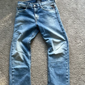Replay ljusblå jeans slim fit - Säljer ett par ljusblå jeans från Replay med klassisk femficksdesign och snygga detaljer på bakfickorna. Jeansen har raka ben och normal passform, tillverkade i mjukt denimtyg. Perfekta för en avslappnad och stilren look.