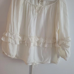 Vit blus med volanger från Ralph Lauren - Supersöt vit blus från Ralph Lauren Denim & Supply i boho-stil. Blusen har långa ärmar, volangdetaljer runt ärmar och midja samt knytning vid halsen. Tillverkad i ett lätt och luftigt tyg som ger en romantisk vibe.