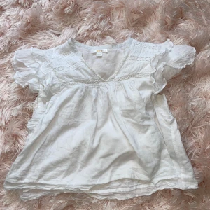 Vit blus med volangärmar - Supersöt vit blus från Gina Tricot med v-ringning och volangiga korta ärmar. Lätt och luftig modell med fina broderade detaljer upptill. Perfekt för en fräsch och somrig look!