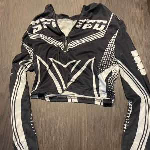 Svart och vit croppad långärmad topp - Säljer en svart och vit croppad långärmad topp med sportig grafik och texten 'SPEED' framtill. Toppen har half zip-dragkedja och coola mönster längs ärmar och kropp. Perfekt för dig som gillar streetstyle och edgy vibes.