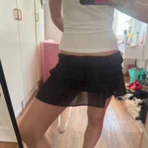 Svart volangkjol  - Skitsöt svart kjol med volanger! Har en liten fläck på baksidan men går förmodligen ut i tvätten men lovar ej något! Vet ej vad storleken är men hade sagt att den passar S-M då den har resår i midjan!