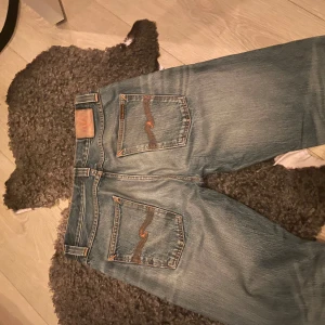 Blå Nudie Jeans med orange sömmar - Säljer ett par klassiska blå jeans från Nudie. Storlek 33/36. Snyggt slitna, litet hål på höger ben.