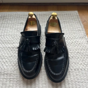 Loafers - Dr Martens - Svarta loafers i äkta läder med tofsar. Klassisk och tidlös modell som passar både till vardag och fest. Endast sparsamt använda och i mycket fint skick. Storlek 42 