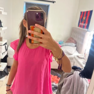 Rosa blus med volangärmar - Säljer en superfin rosa blus med volangärmar och rund halsringning. Blusen har en lös passform och är tillverkad i ett tunt, flowy material som ger en luftig känsla. Perfekt för dig som gillar färg och vill sticka ut lite extra.