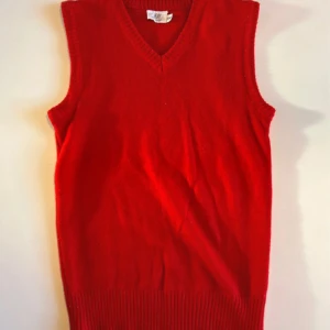 Röd stickad väst från H&M - Riktigt snygg röd stickad väst från H&M med v-ringad hals och ribbade kanter. Perfekt att slänga över en skjorta eller t-shirt för en cool lager-på-lager-look. Tillverkad i 100% akryl för en mjuk och bekväm känsla.